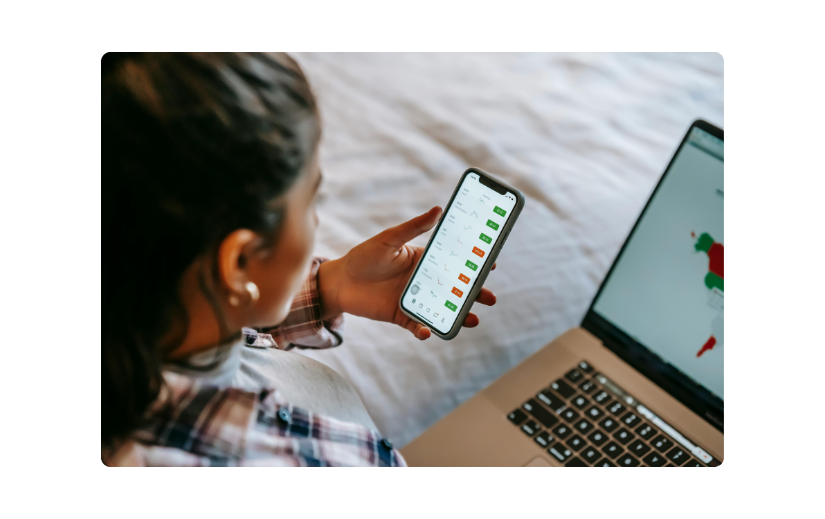 Woman engaging in mobile shopping on her smartphone while using a laptop, highlighting the rise of mCommerce in 2025.